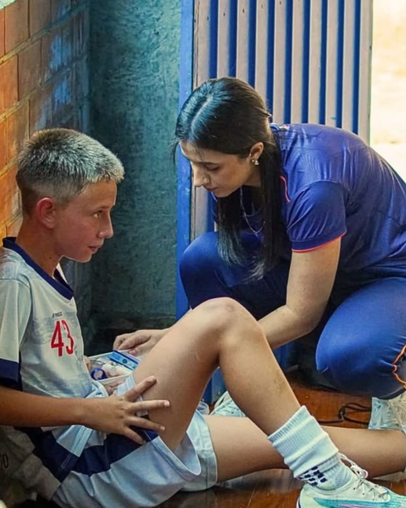 Bruna Pimentel Pahim atendendo o joelho de um jovem atleta na beira da quadra